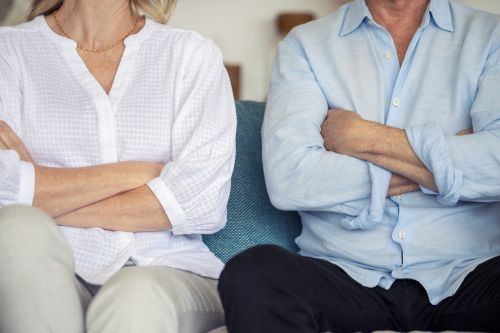 Mature couple sitting on the sofa. They are both angry and have their arms crossed. They are concerned with protecting inheritance in an Ohio Divorce.